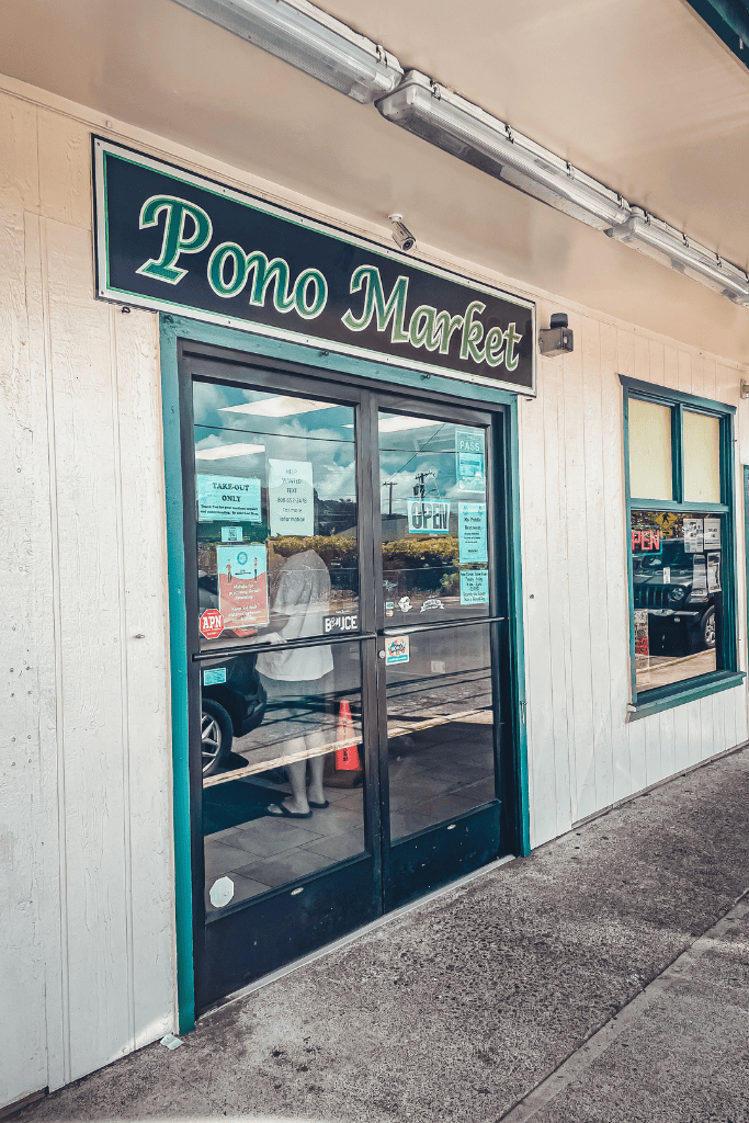 The entrance of Pono Market in Kapaa, a popular local stop for authentic Hawaiian takeout, with reflection of a customer on the glass door.