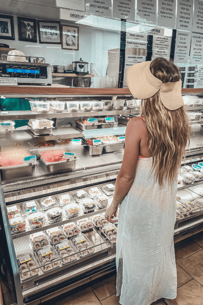 Kate browses a deli case packed with fresh poke, sushi, and traditional Hawaiian foods inside Pono Market.