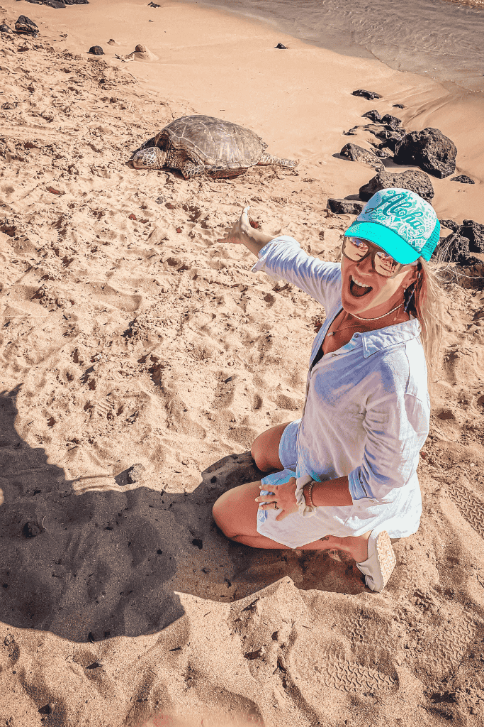 Kate beams with excitement as she kneels and points toward a Hawaiian green sea turtle resting peacefully on the golden sand.