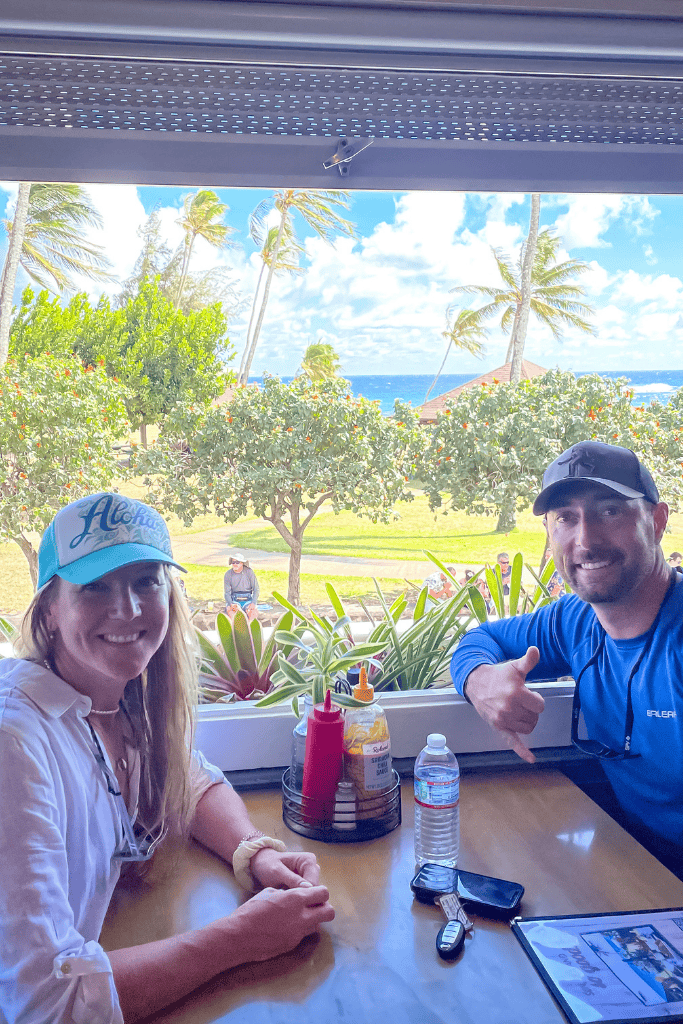 Kate and her husband smile from a window-side table at Brennecke’s with a view of palm trees, the ocean, and blue skies just beyond the open window.