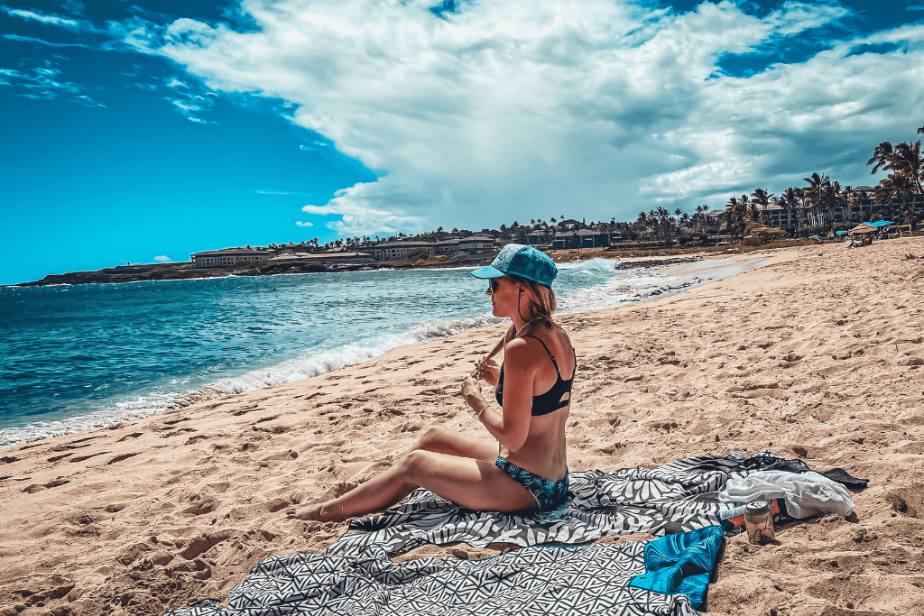 Kate relaxes on a patterned beach towel at Shipwreck Beach, soaking in the coastal breeze with palm trees lining the background.
