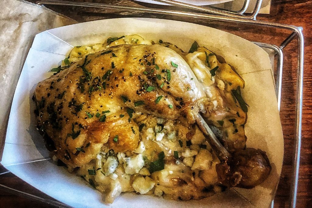 A plate of savory duck confit served over a bed of creamy gnocchi, topped with fresh herbs and crumbled cheese. The dish is presented in a rustic, farm-to-table style at a Vermont restaurant, showcasing locally sourced ingredients.