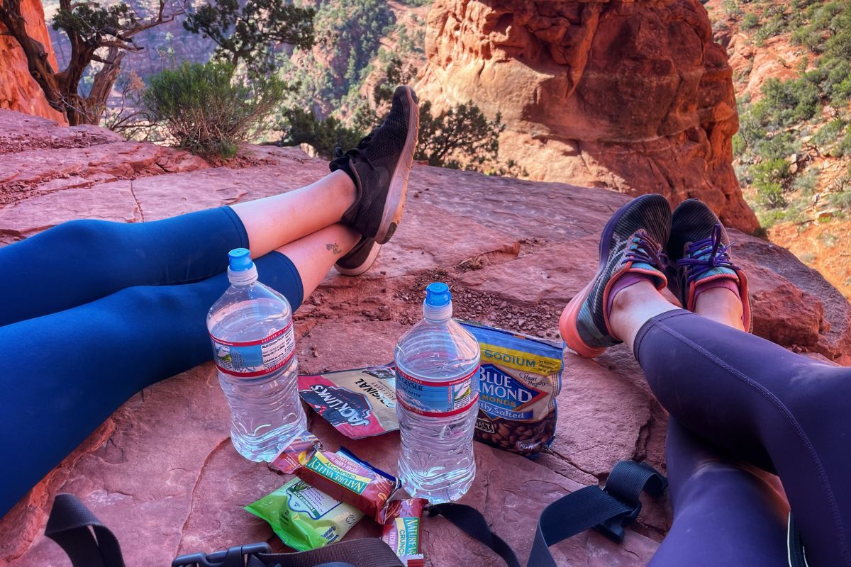 Kate taking a break during the hike up Cathedral Rock, with snacks and water bottles spread out on the rocky surface and stunning views in the background.