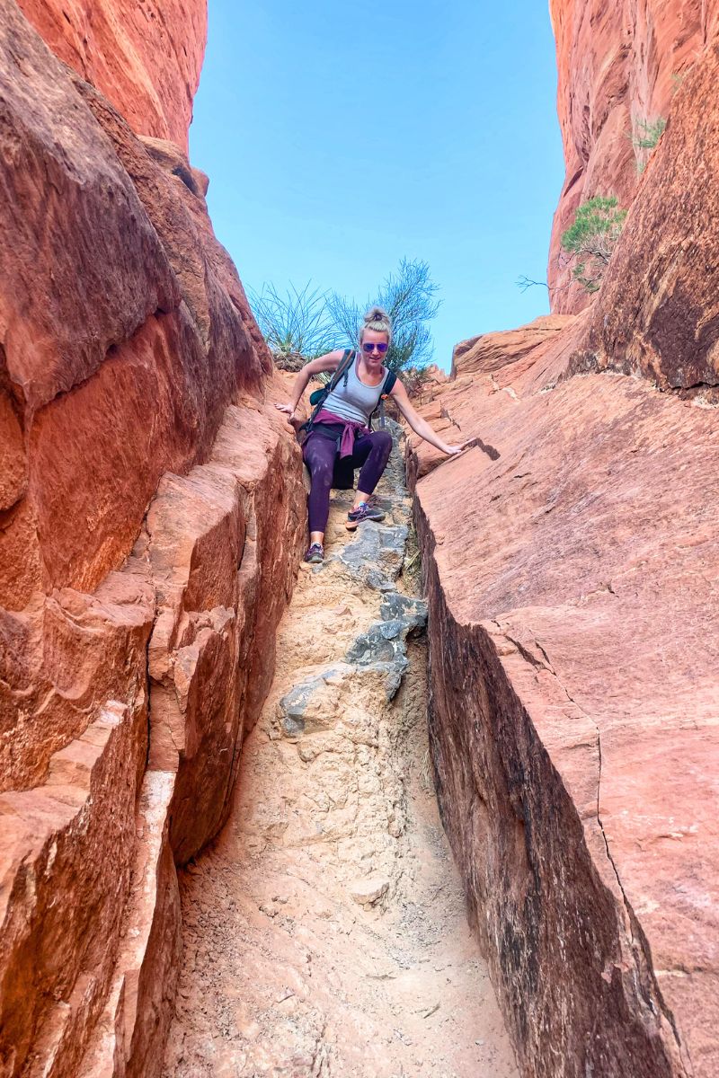 Kate carefully navigates a narrow, rocky path between towering red rock walls at Cathedral Rock in Sedona.