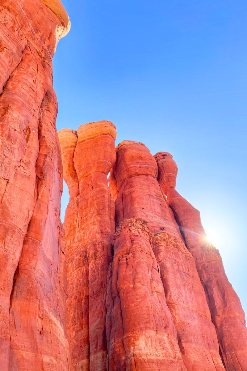 A close-up view of the towering red rock formations of Cathedral Rock in Sedona, with the sun peeking from behind, highlighting the vibrant colors against a clear blue sky.