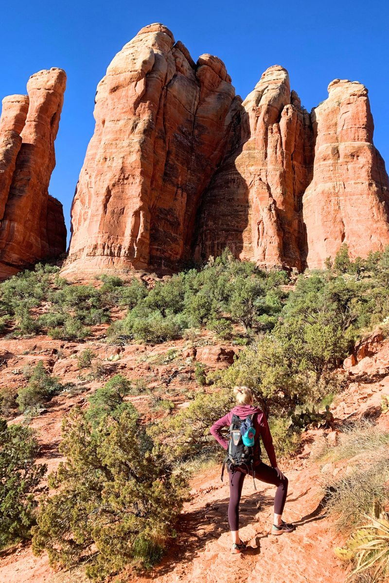 Kate standing on the Cathedral Rock Trail in Sedona, looking up at the towering red rock formations against a clear blue sky, ready to continue her hike.