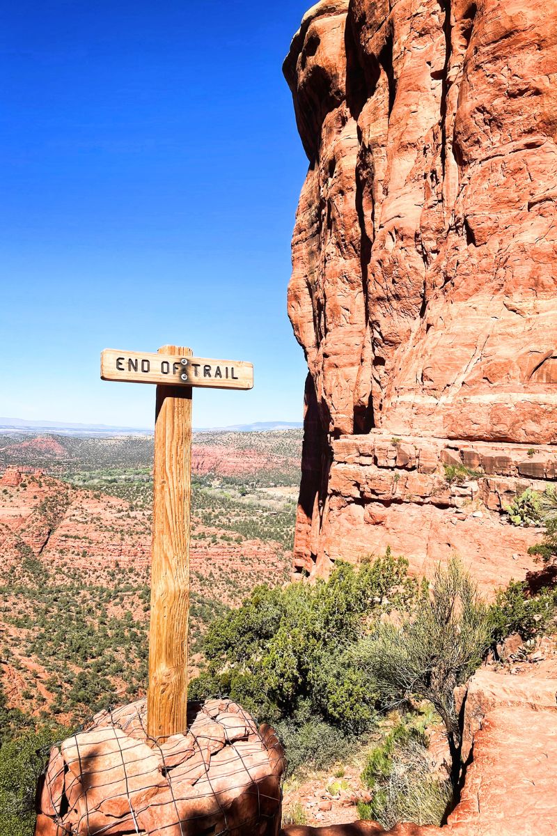 "End of Trail" sign on Cathedral Rock Trail in Sedona, surrounded by red rock formations and overlooking a scenic valley under a bright blue sky.