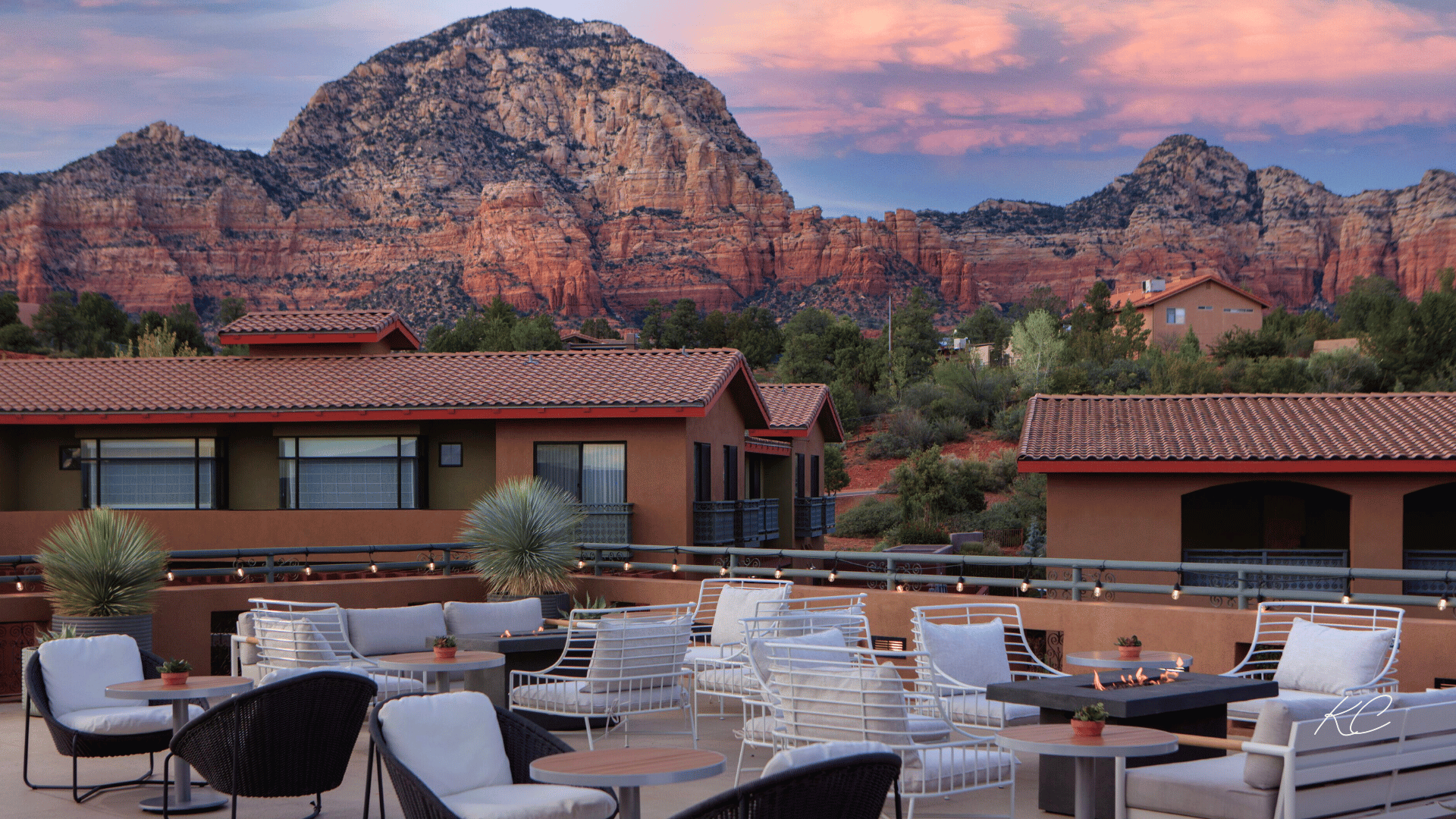 An outdoor terrace with comfortable seating around a fire pit, set against the backdrop of Sedona's stunning red rock formations under a colorful sunset sky.