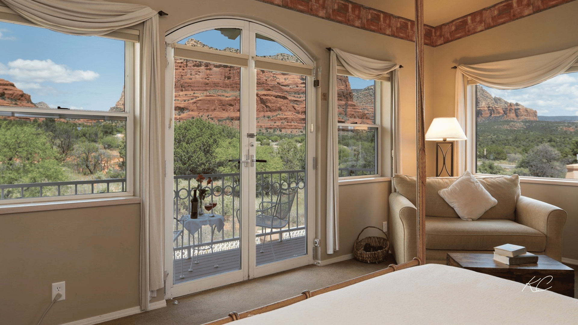 A cozy hotel room in Sedona with large windows and a balcony, offering breathtaking views of the iconic red rock formations and lush greenery.