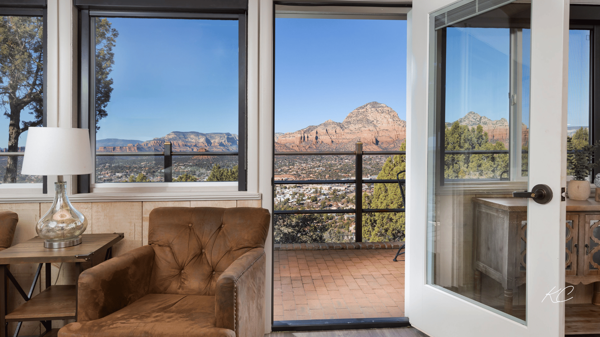 A luxurious hotel room in Sedona featuring large windows and a balcony with stunning views of the red rock mountains and the town below.