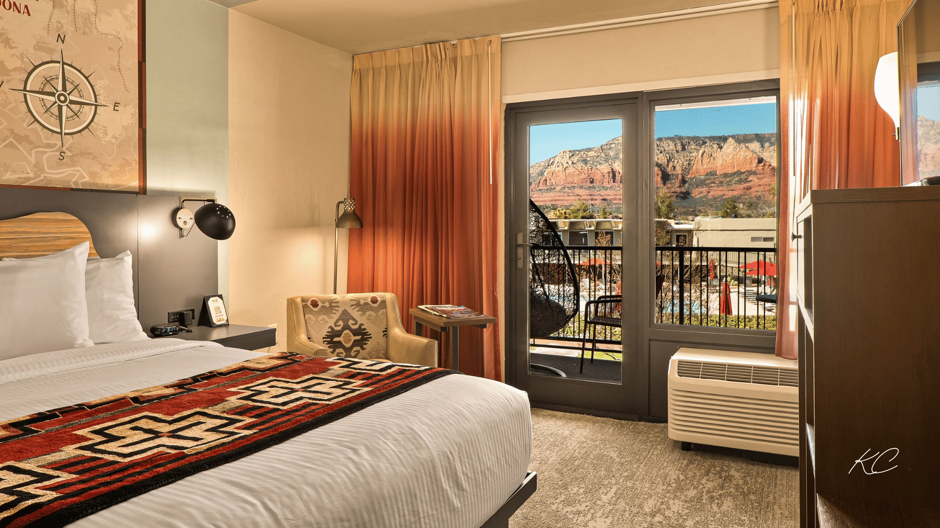 A stylish hotel room in Sedona with a Southwestern-themed blanket, a cozy seating area, and a balcony offering stunning views of the red rock formations.