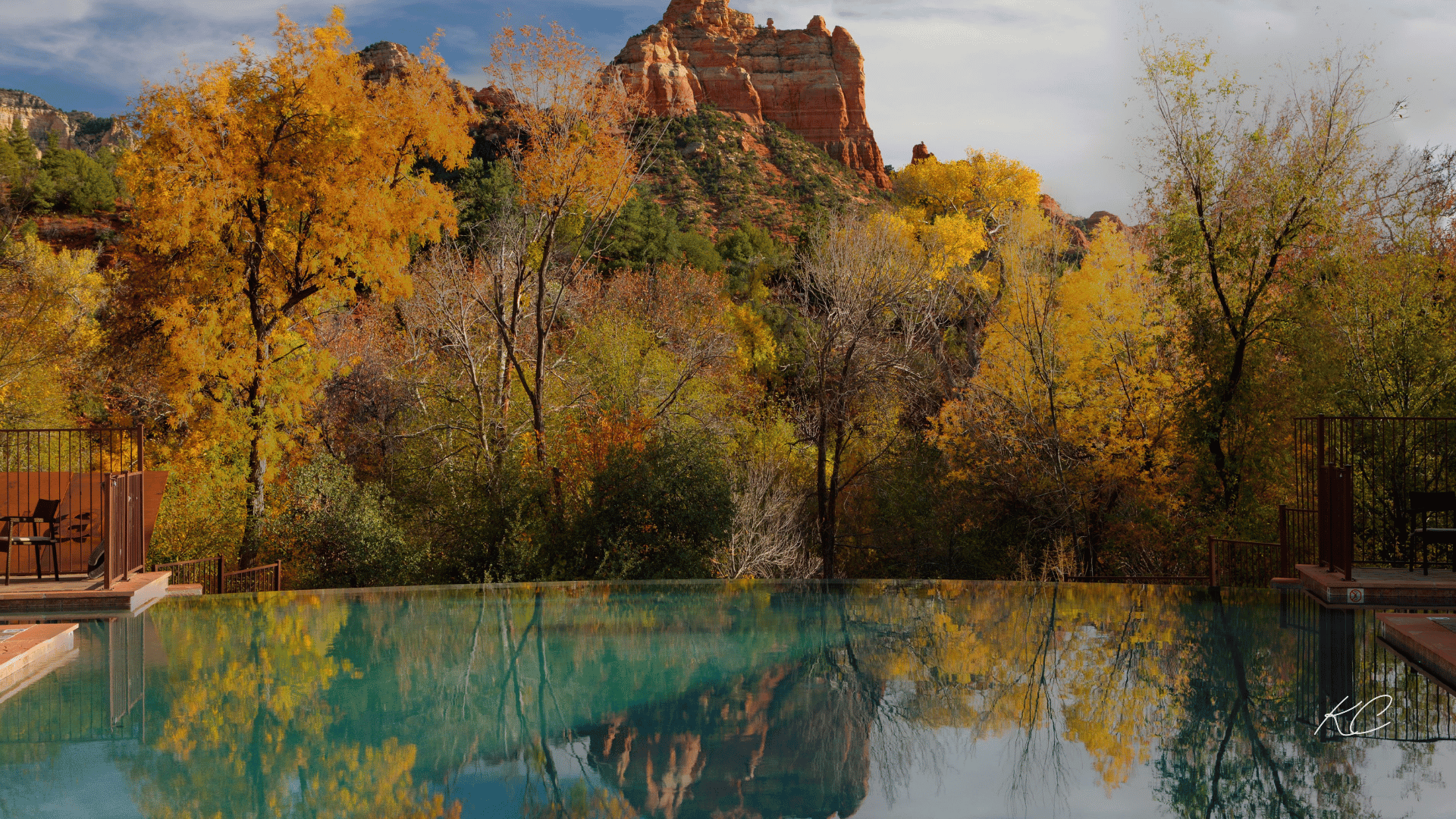 A tranquil pool reflecting the vibrant fall foliage and the iconic red rock formations of Sedona in the background.