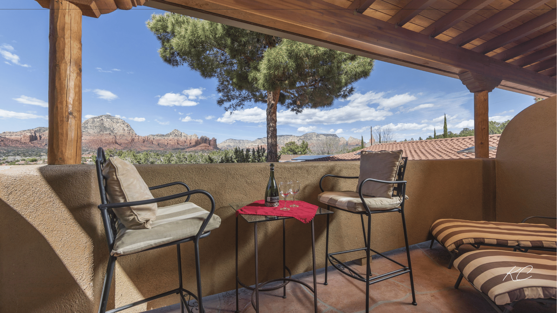 A cozy patio with cushioned chairs and a table set for drinks, offering stunning views of Sedona's red rock formations and a clear blue sky.