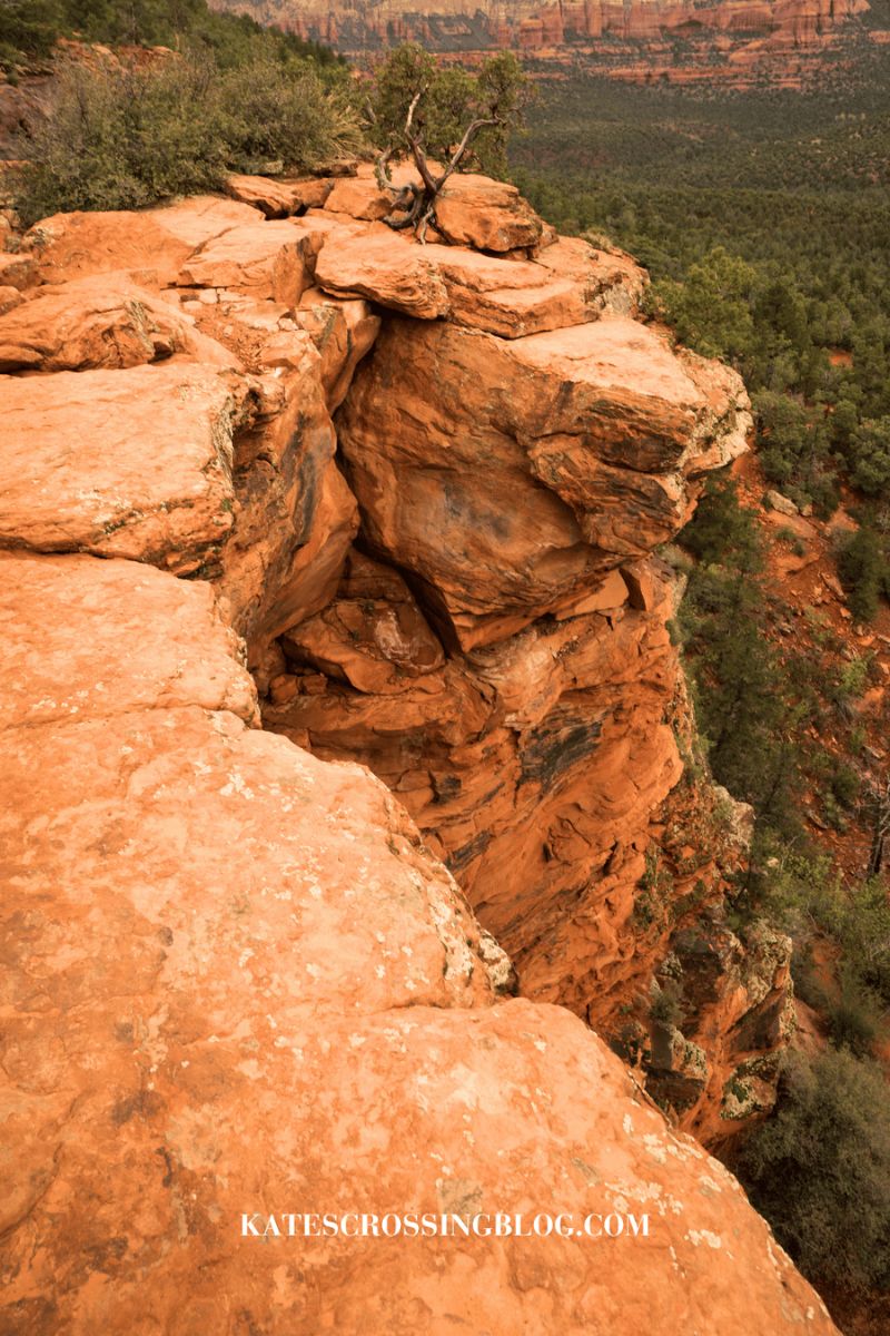 A close-up view of the rugged red rock formations of Devil's Bridge, highlighting the steep drop and the natural beauty of the surrounding Sedona landscape.