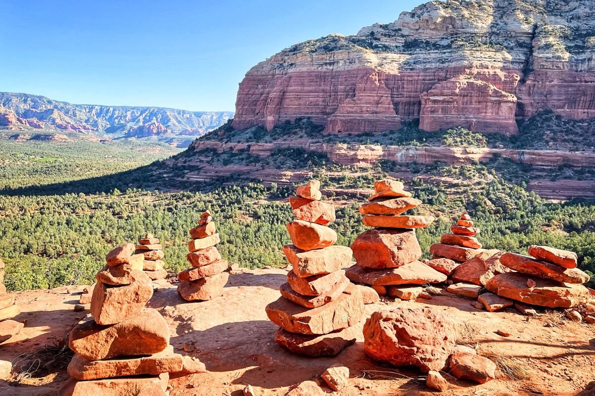 Cairns marking the trail on the Devil's Bridge hike, with stunning red rock formations and a lush green valley in the background.