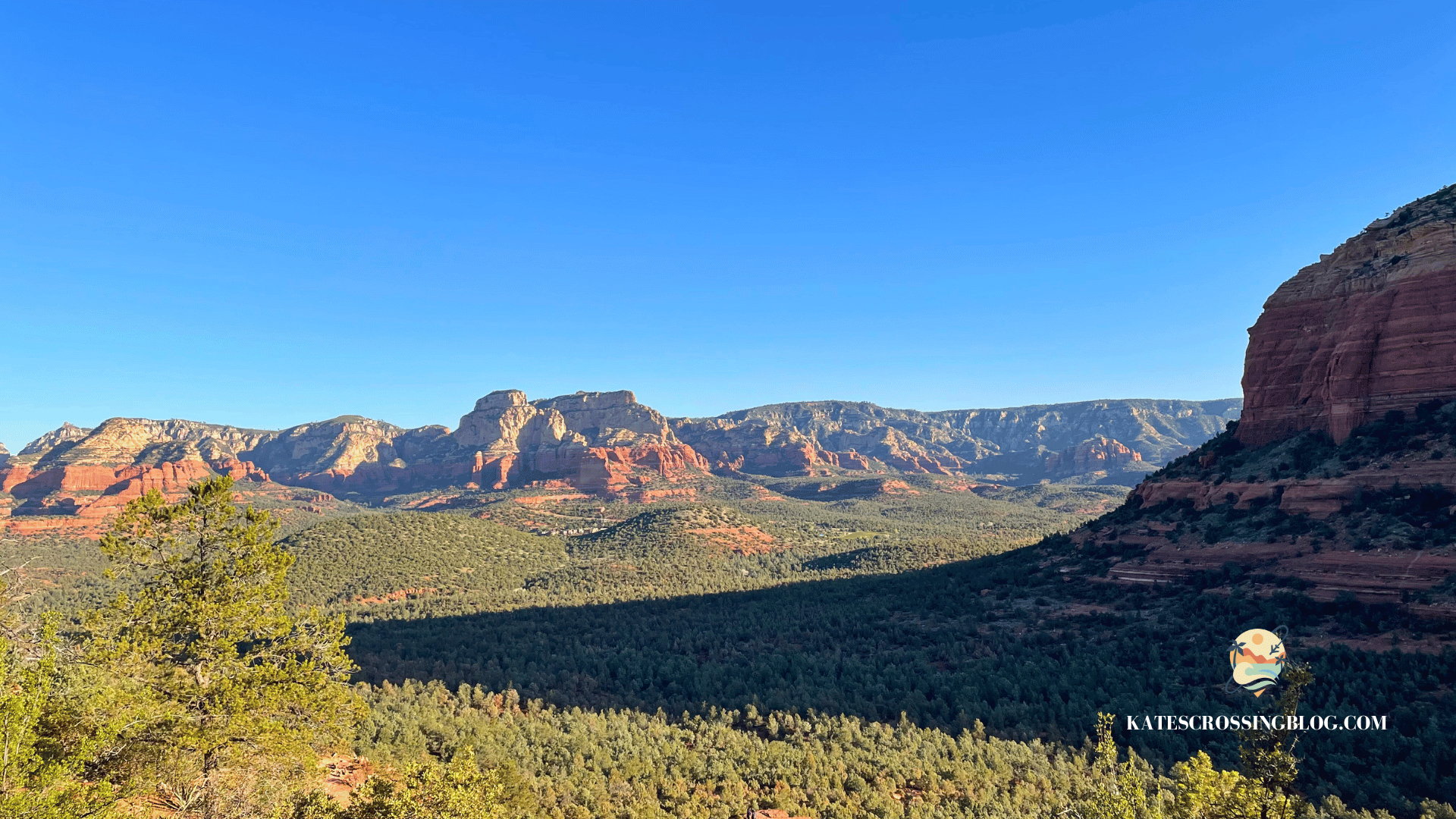 A panoramic view of Sedona's red rock formations and green forests under a clear blue sky.