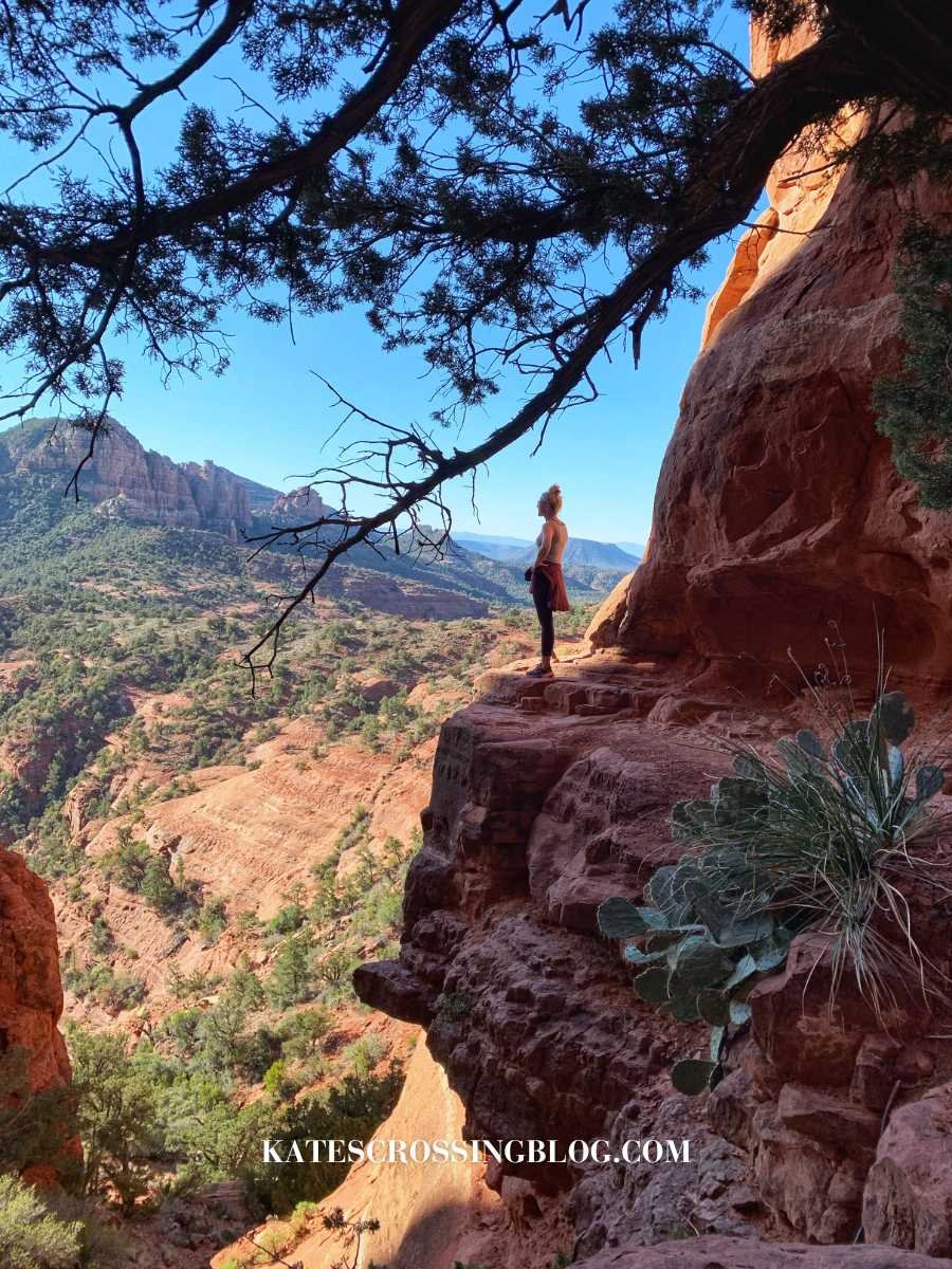 Cover photo for blog post: Best Hikes in Sedona. I'm standing on a rock ledge at the top of Cathedral Rock, looking out over the desert landscape of Sedona Arizona.