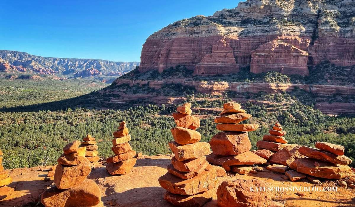 Picture of cairns which are a pile of stacked rocks along the trail leading up to Devils Bridge. There is a view of desert landscape and red rock formations in the back ground. The day is sunny with a blue bird sky.