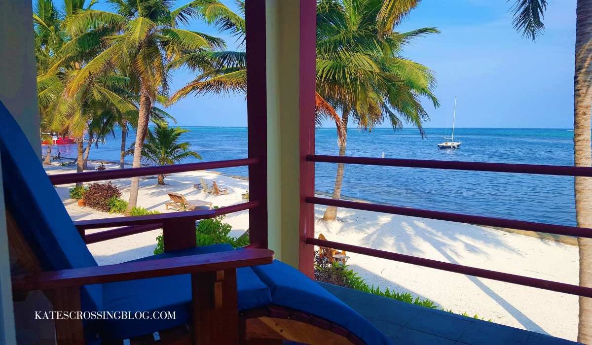 Balcony view from a beach front room of Tres Cocos Resort. The balcony has lounge chasers that look out at turquoise waters and a white sand beach with palm trees.