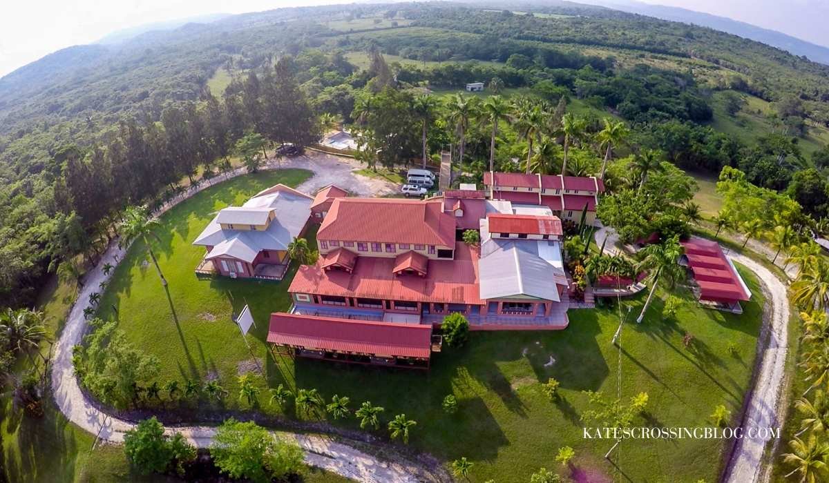 arial view of Rumors Resort Hotel and its ground surrounded by jungle. The roofs are a clay red color and the the lawns are pristine. A driveway encircles the entire resort.