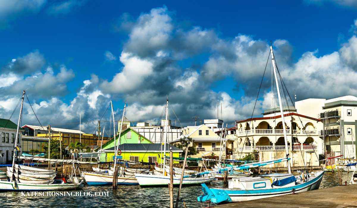 View of Belize city water port filled with small sail boats and lots of older buildings along the shore in the back ground. The buildings look old and ran down and stacked on top of each other.