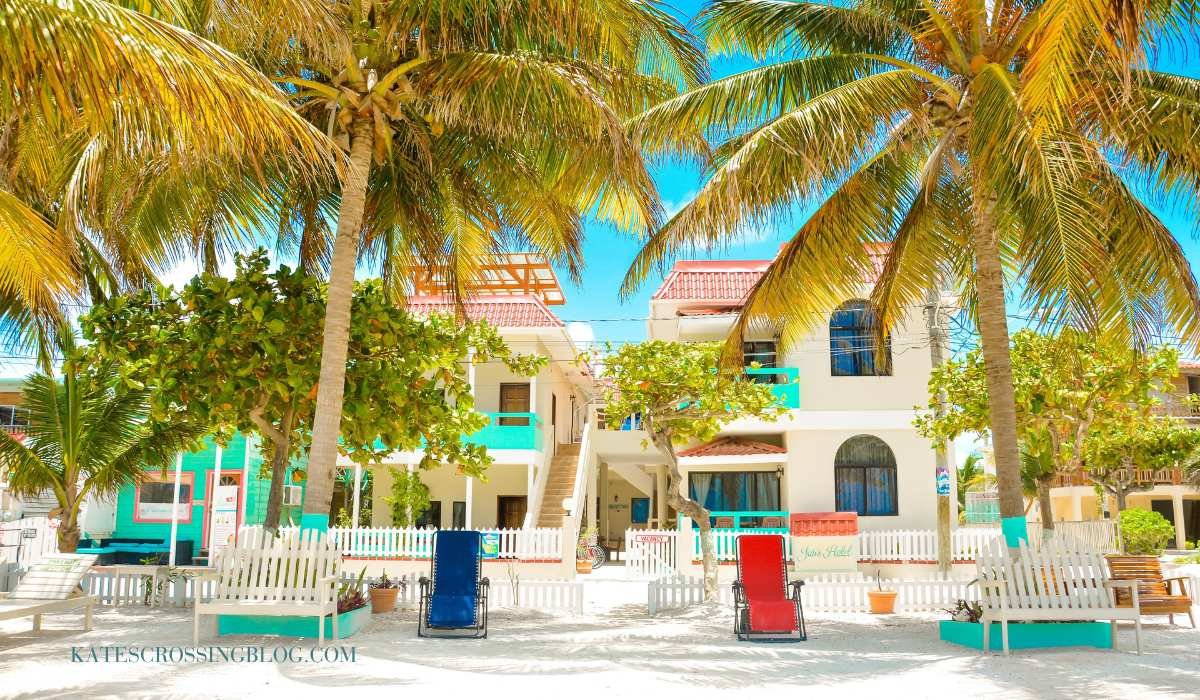 image of Jan's Hotel front view. Looking at it from the beach out front there are beach chairs and palm trees framing the hotel. The hotel is a white two story hotel with turquoise balconies for the rooms in the front.