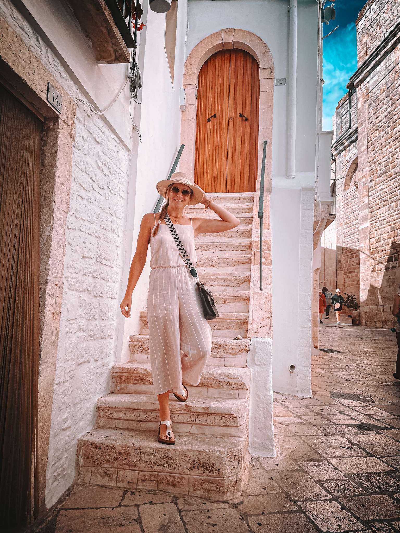 Kate from Kate's Crossing Blog exploring a charming stone street, wearing a stylish hat and sunglasses, embodying her adventurous spirit.