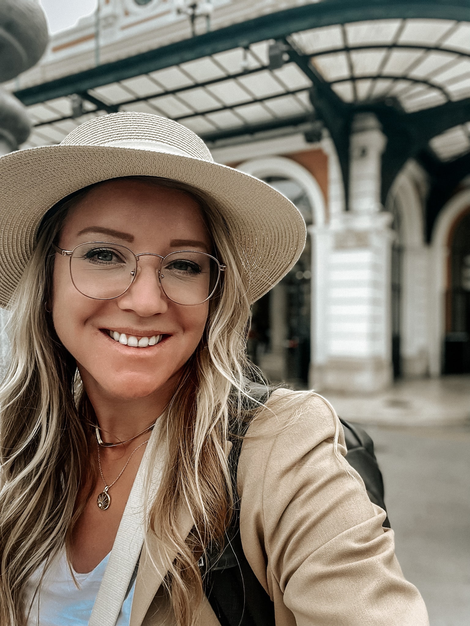 Kate, the owner of Kate's Crossing Blog, smiling while wearing a hat and glasses, with a travel backdrop behind her.