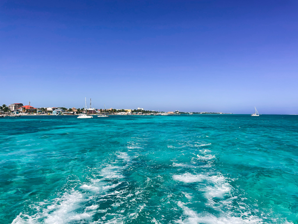 View of Belize's coastline from a water taxi, showcasing the vibrant blue waters and sailboats, capturing the essence of island hopping in Belize.