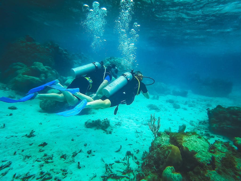 Kate and her husband scuba diving together in the clear waters of Belize, exploring the vibrant coral reefs and marine life, showcasing a key activity to prepare for with travel insurance.