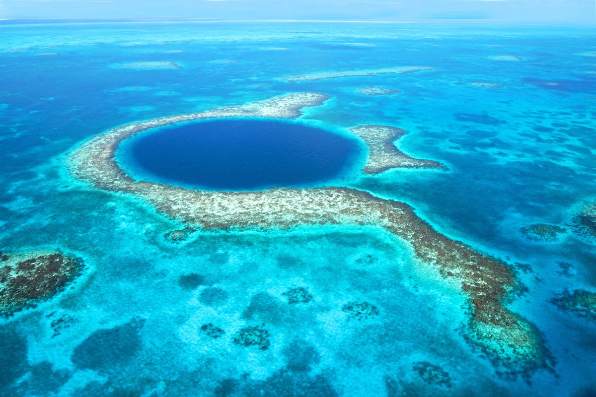 Aerial view of the Great Blue Hole in Belize, showcasing a large, deep blue circular sinkhole surrounded by vibrant turquoise waters and coral reefs.