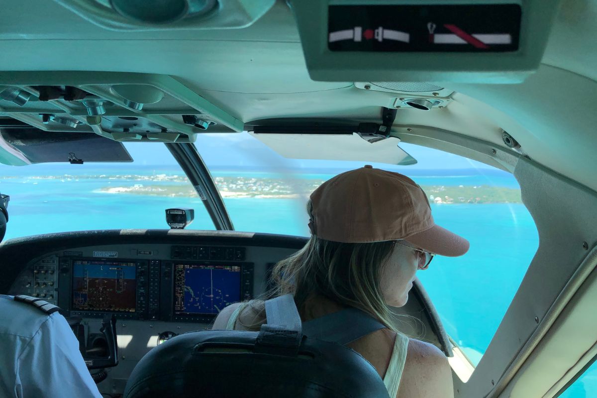 Kate sitting in the cockpit of a small plane, looking out at the turquoise waters and islands below as she flies to Caye Caulker, Belize.