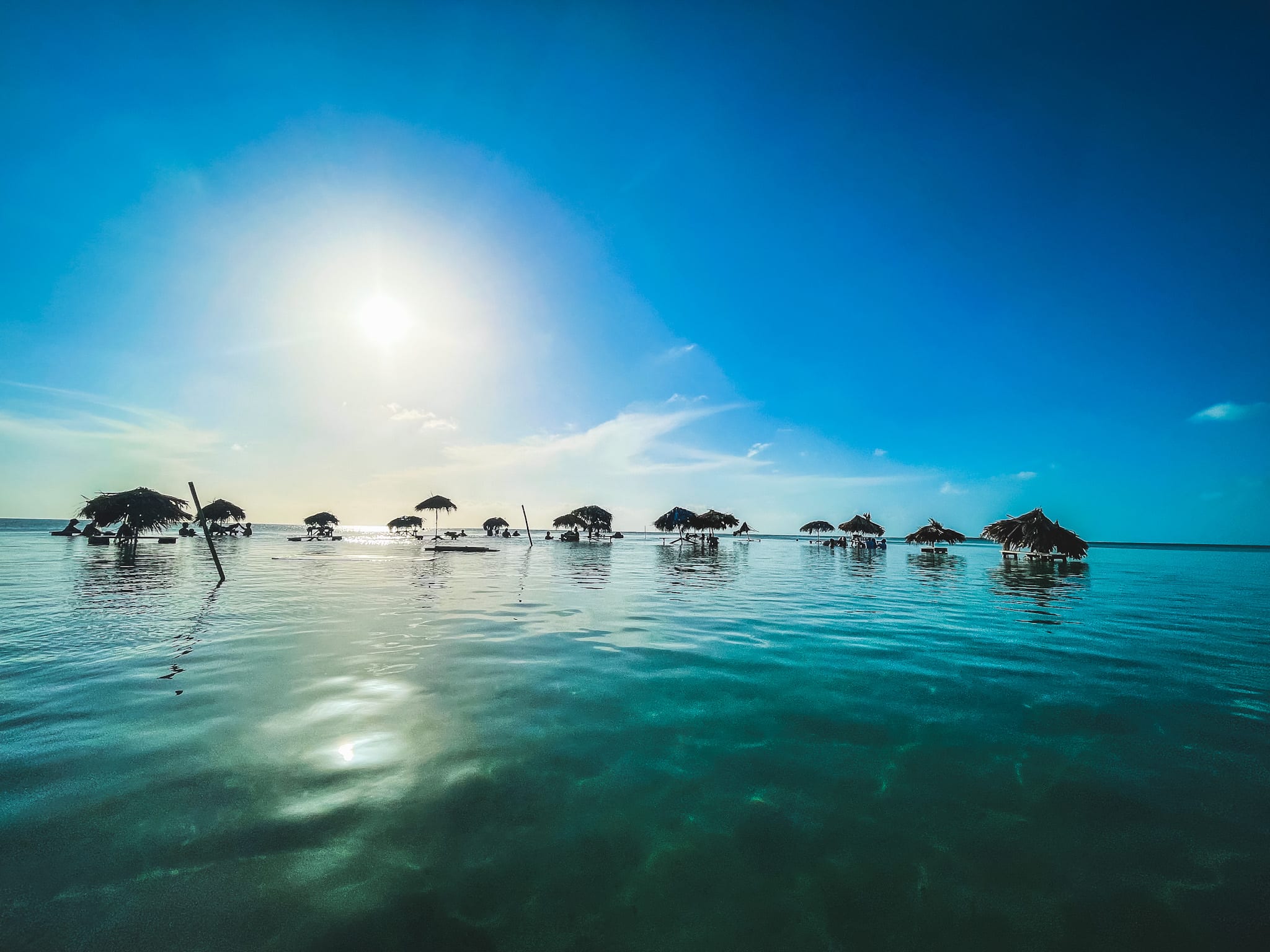 Thatch covered cabanas out in the turquoise Belize waters with sunsetting.