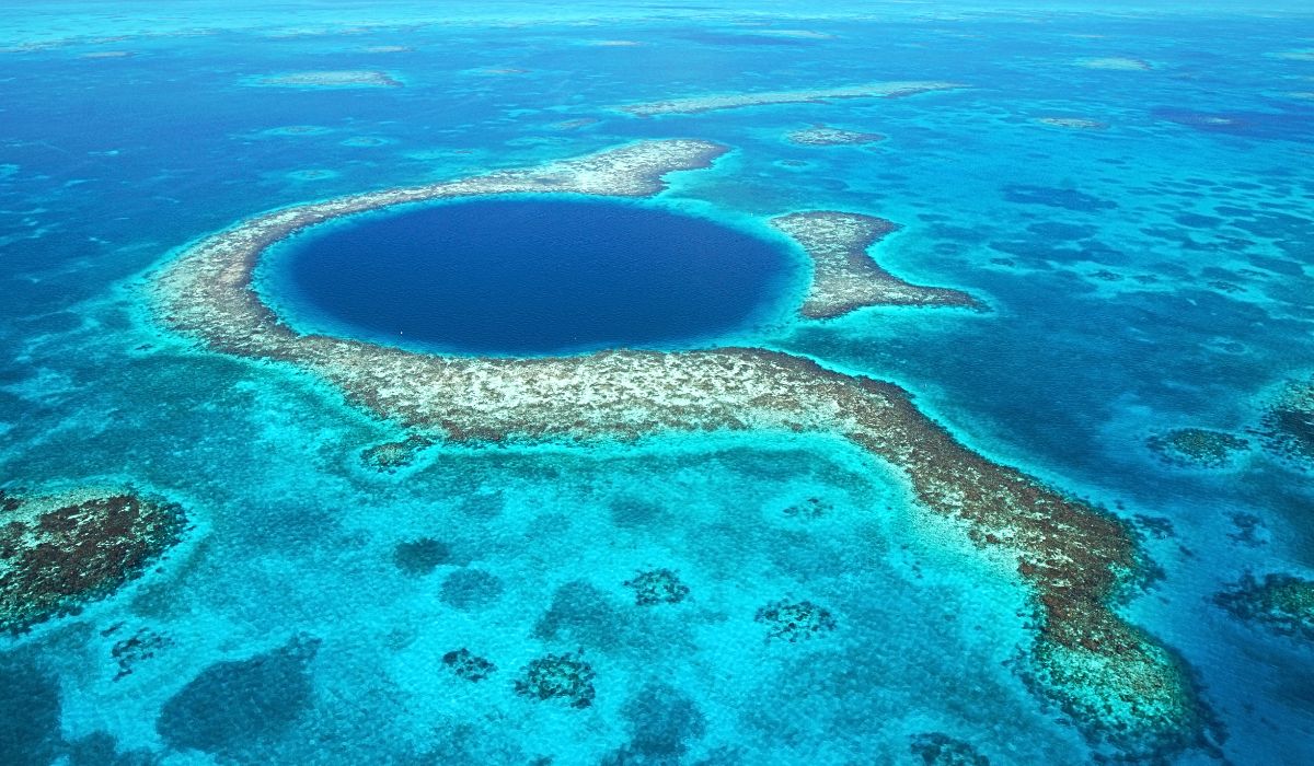 Aerial view of the Great Blue Hole near Caye Caulker, Belize, showcasing the stunning deep blue circular sinkhole surrounded by vibrant turquoise waters and coral formations.