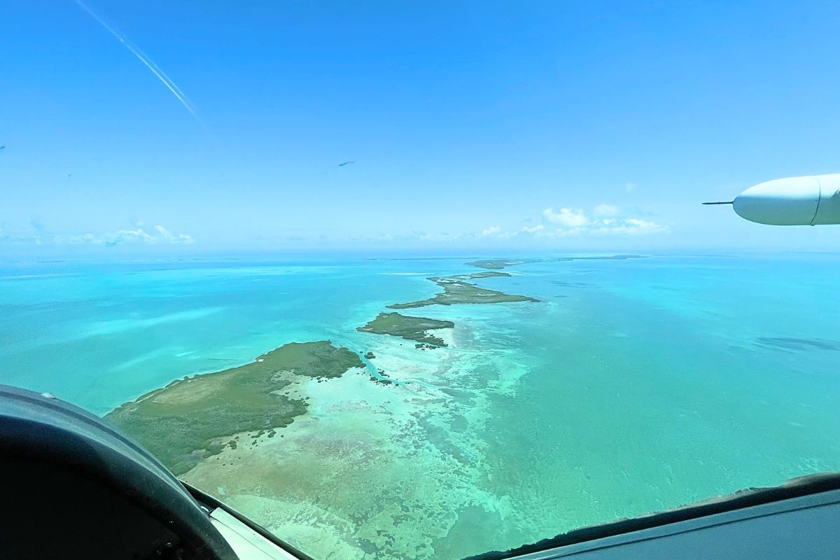 Aerial view from a plane flying over the turquoise waters and small islands of Belize under a clear blue sky.