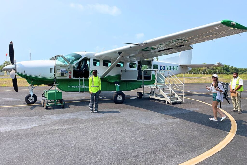 Kate boarding a small Maya Island Air plane on the tarmac with two ground crew members in safety vests nearby and its a sunny blue sky day. 