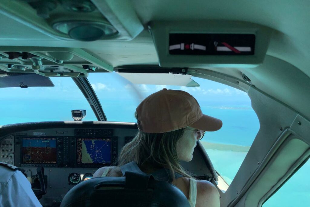 Kate on a domestic flight to the Cayes of Belize, as featured in a Belize Travel Guide, wearing a cap and looking out the window at the turquoise waters below