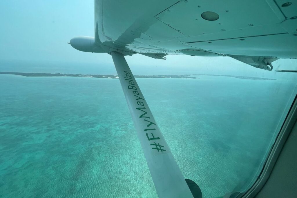 View from a domestic flight to the Cayes of Belize, showing the turquoise waters below and part of the airplane wing.