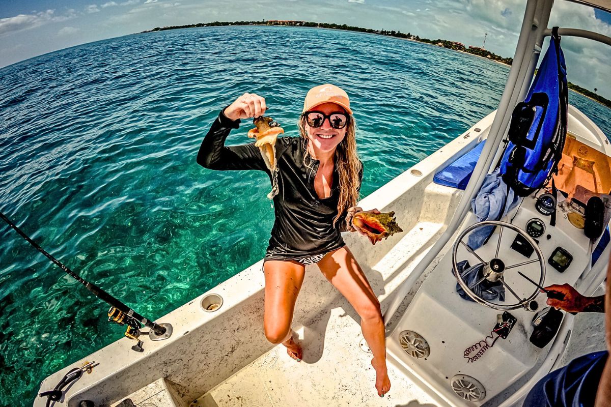 Kate learning to clean conch shells on a boat in Belize. She is holding up the conch meat and smiling.