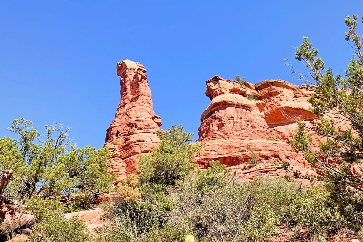 View of the Boynton Canyon Vortex, a striking red rock formation surrounded by lush greenery under a clear blue sky in Sedona.