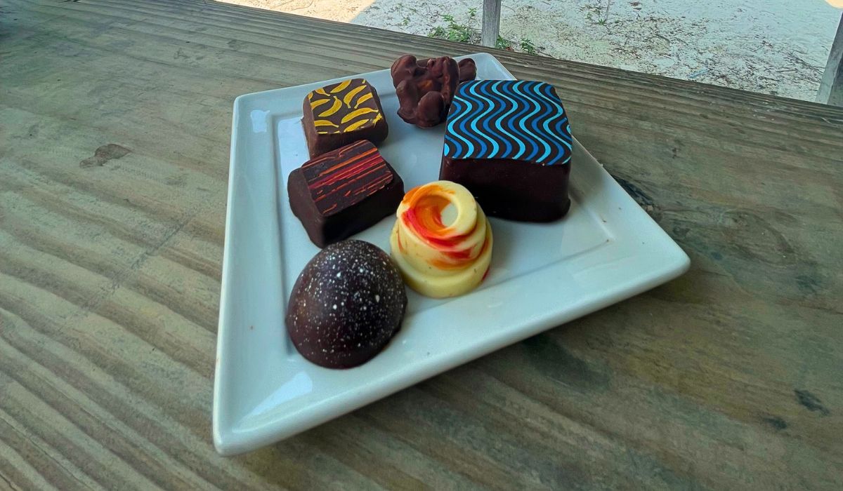 A plate of assorted Belizean chocolates, each piece uniquely decorated with colorful patterns and designs. The chocolates include a variety of shapes and fillings, showcasing the artisanal craftsmanship and rich cacao heritage of Belize.