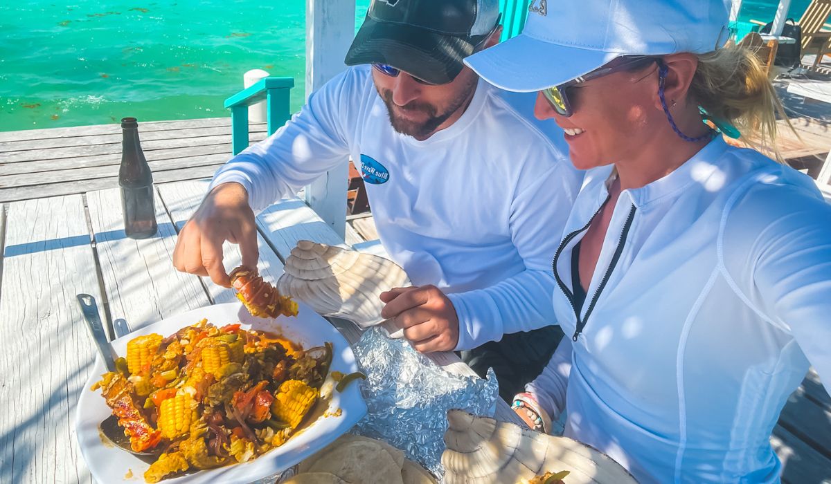 Kate and her husband enjoy a delicious seafood feast at an outdoor table overlooking the turquoise waters of Belize. The plate is filled with fresh lobster, corn, and other vibrant ingredients, capturing the essence of Belizean cuisine.