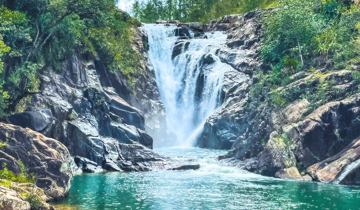 A stunning waterfall cascades down rugged, rocky cliffs surrounded by lush greenery, creating a serene pool of turquoise water at its base. This is Big Rock Falls, a popular natural attraction in San Ignacio, Belize.