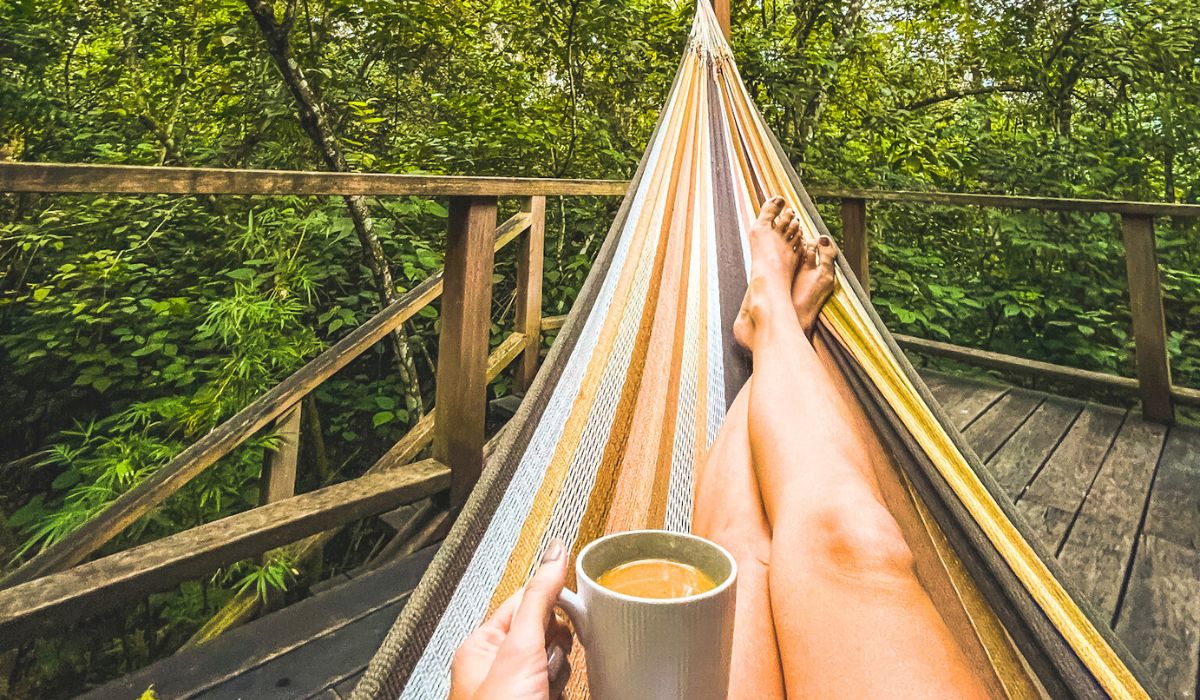 Kate relaxing in a hammock with a cup of coffee, surrounded by the lush greenery of the jungle at Vanilla Hills Lodge.