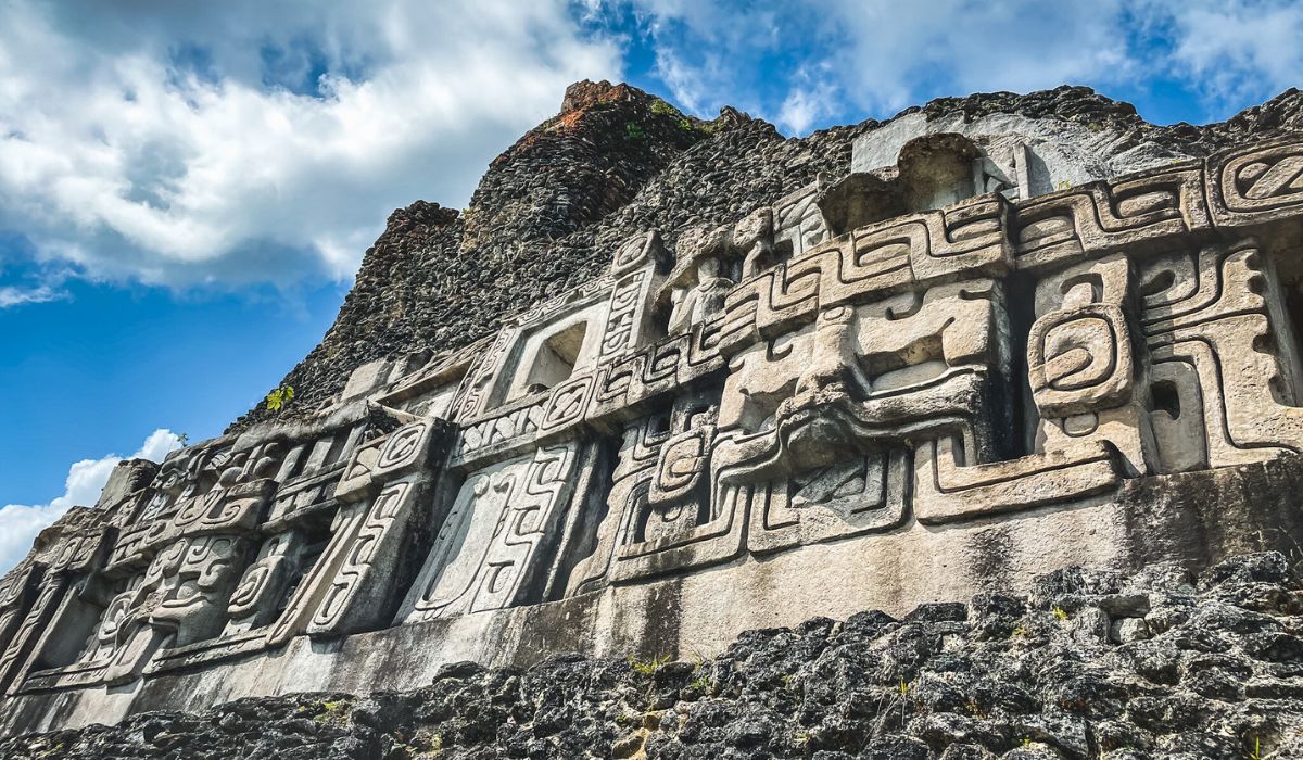 the ancient stone carvings at Xunantunich Mayan Ruins, one of the top things to do in San Ignacio, Belize, with intricate patterns and figures against a backdrop of blue sky and clouds.