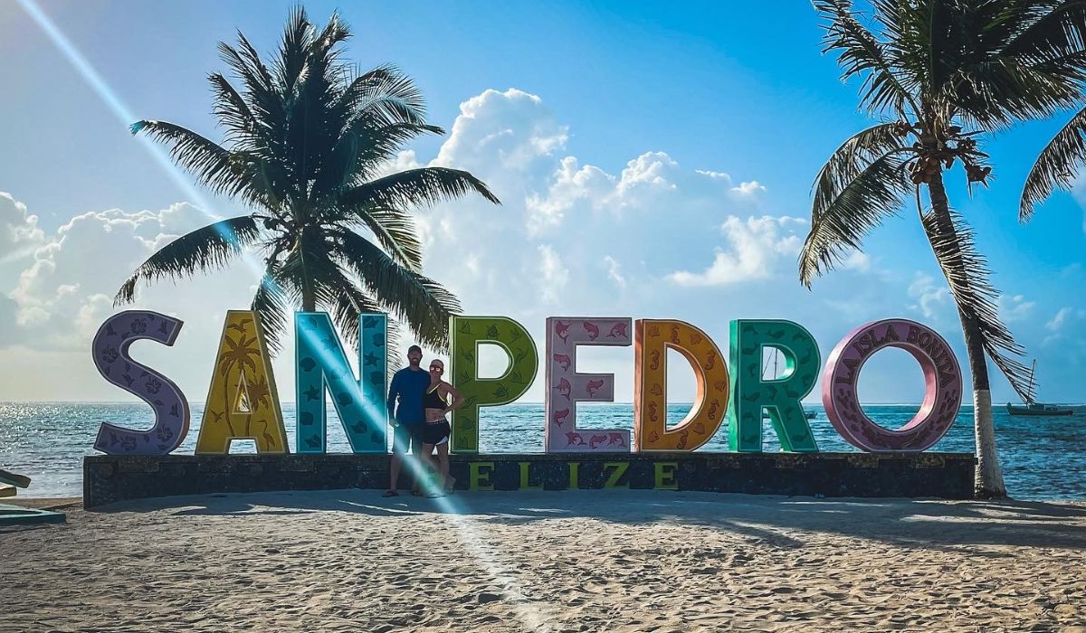 Kate and her husband pose in front of the colorful 'San Pedro' sign on the beach, framed by palm trees and the Caribbean Sea, highlighting one of the top things to do in San Pedro, Belize.