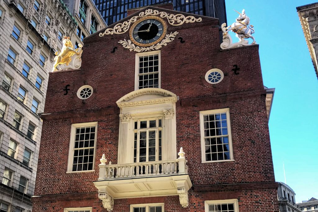 Close-up of the historic Old State House in Boston, featuring its red-brick facade, intricate golden accents, and statues against a backdrop of modern buildings.