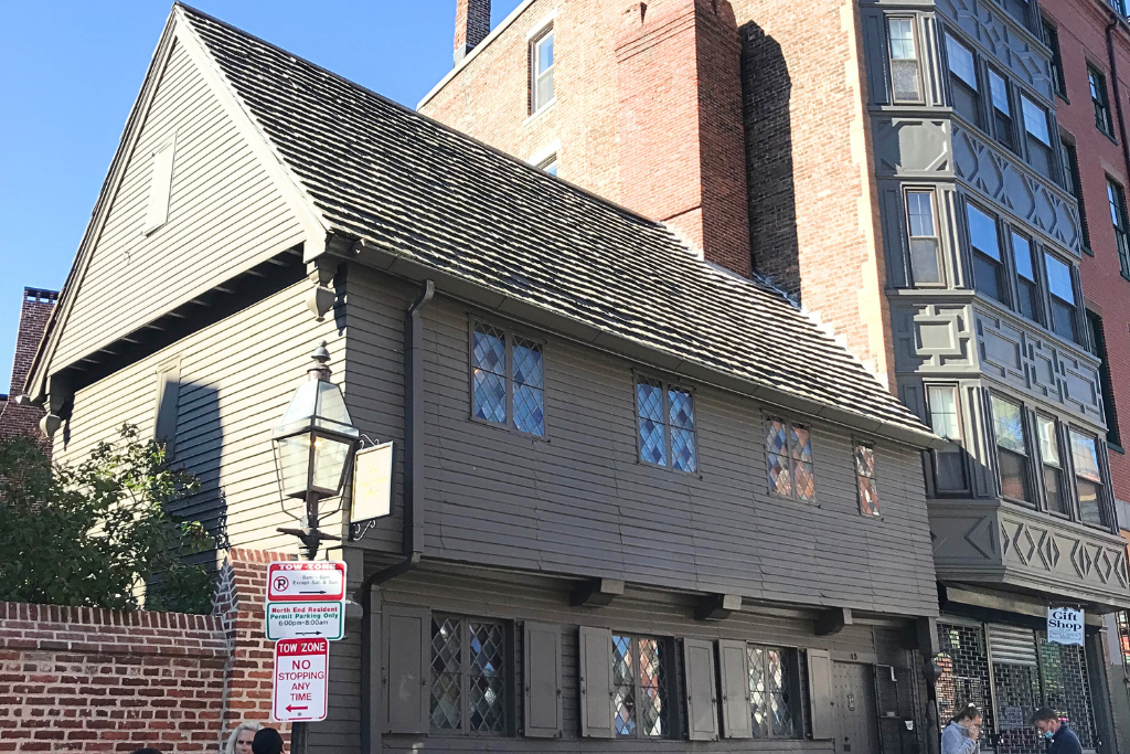 Exterior view of the Paul Revere House in Boston, a historic wooden structure with diamond-patterned windows and a sloped roof, contrasting with modern brick and glass buildings nearby. A popular stop along Boston’s Freedom Trail.