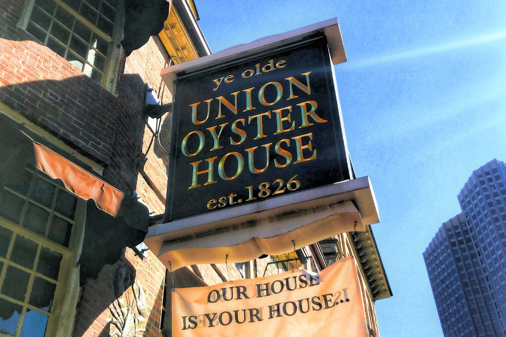 Sign for the historic Union Oyster House in Boston, established in 1826, displayed on the side of a brick building under a clear blue sky, with the slogan 'Our House is Your House' hanging below, showcasing one of the city's oldest and most famous restaurants.