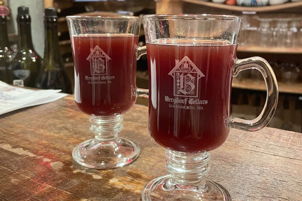 This image shows two clear glass mugs filled with a warm red beverage, likely mulled wine, served at Bergdorf Cellars in Leavenworth, Washington. The mugs feature the winery's logo and are set on a rustic wooden countertop. The cozy, inviting presentation suggests a winter or holiday setting, perfect for enjoying warm drinks in the heart of Leavenworth's festive atmosphere.








